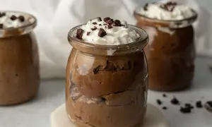Czekoladowy pudding proteinowy w słoiczku, udekorowany bitą śmietaną i kawałkami czekolady.