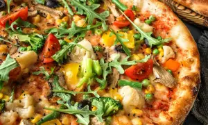 Zbliżenie na wegetariańską pizzę z brokułami, pomidorami, papryką, kukurydzą i rukolą.