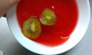 Dwa plastry kiwi w czerwonej galaretce w białej misce.