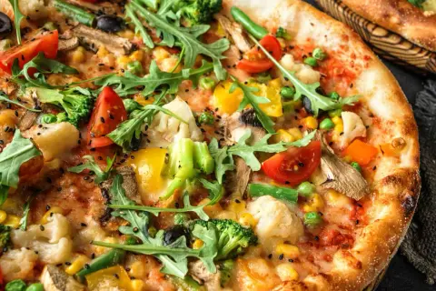 Zbliżenie na wegetariańską pizzę z brokułami, pomidorami, papryką, kukurydzą i rukolą.
