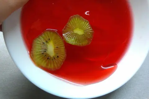 Dwa plastry kiwi w czerwonej galaretce w białej misce.