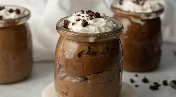Czekoladowy pudding proteinowy w słoiczku, udekorowany bitą śmietaną i kawałkami czekolady.