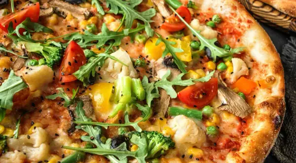 Zbliżenie na wegetariańską pizzę z brokułami, pomidorami, papryką, kukurydzą i rukolą.