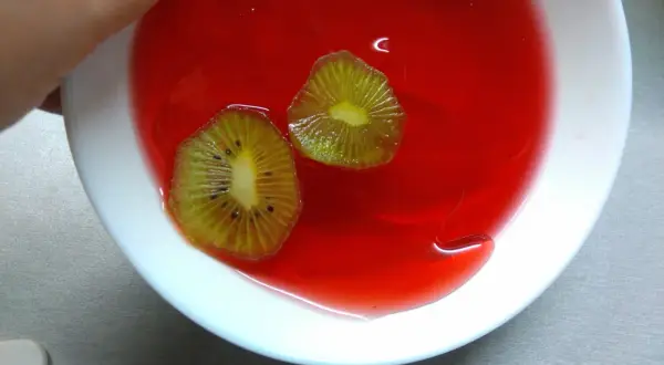 Dwa plastry kiwi w czerwonej galaretce w białej misce.
