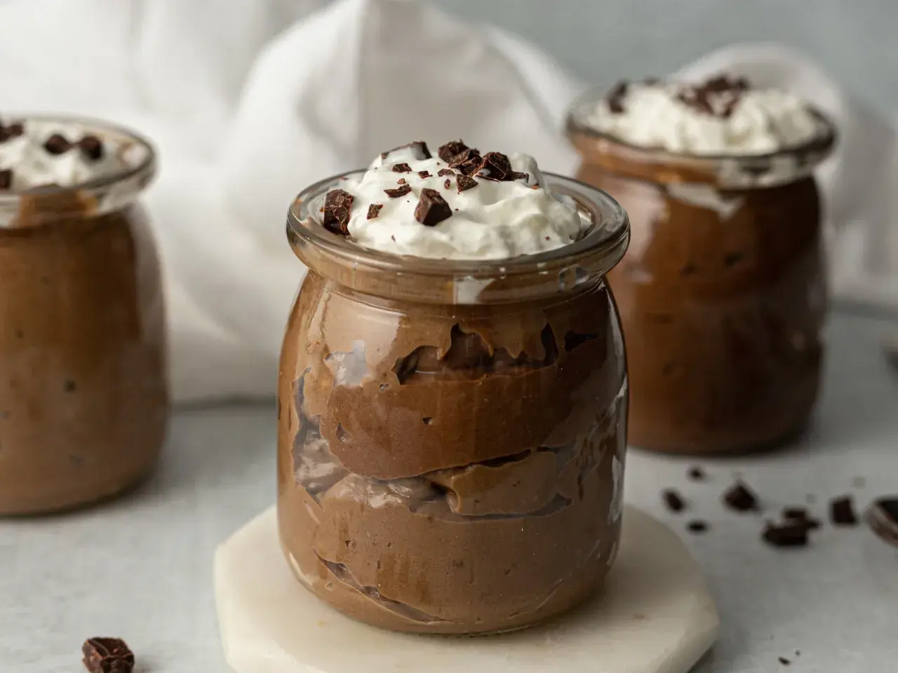Czekoladowy pudding proteinowy w słoiczku, udekorowany bitą śmietaną i kawałkami czekolady.