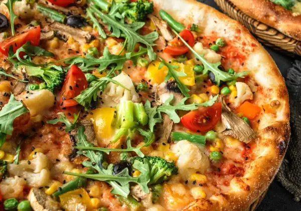 Zbliżenie na wegetariańską pizzę z brokułami, pomidorami, papryką, kukurydzą i rukolą.